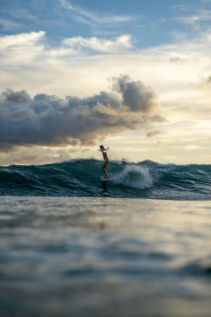 Surfer riding a wave under a cloudy sky at sunrise or sunset