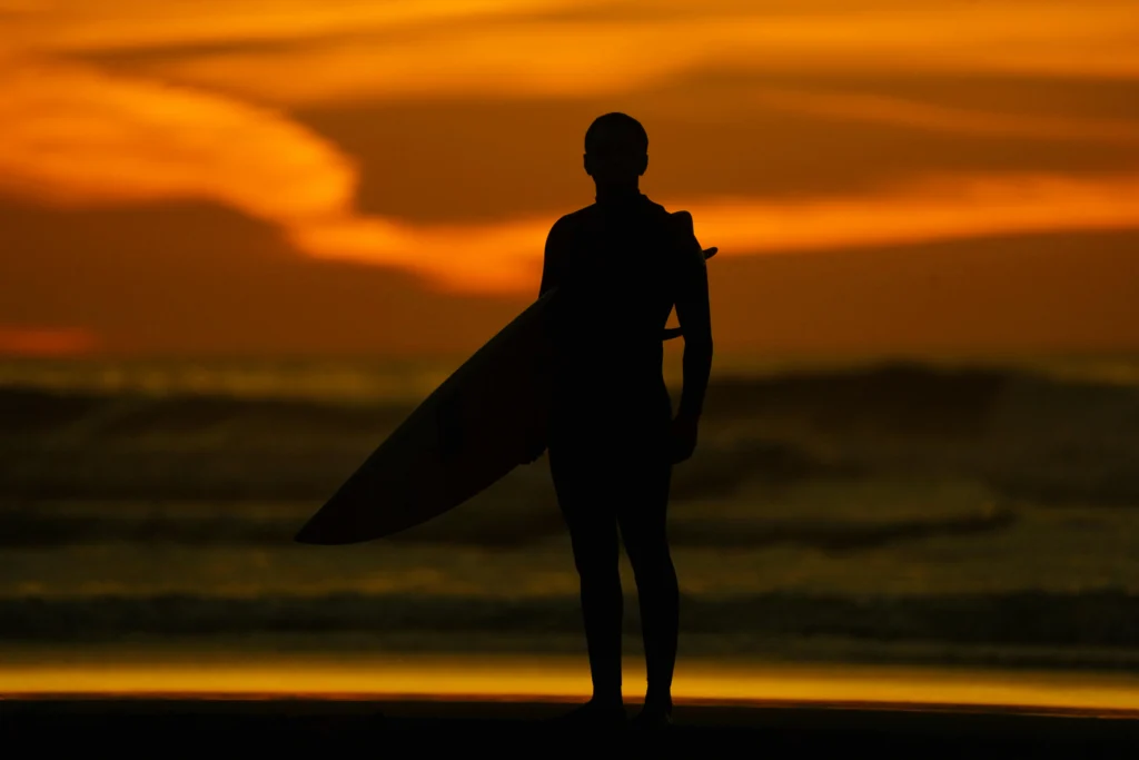 Silhouette of a surfer holding a surfboard at sunset on the beach.